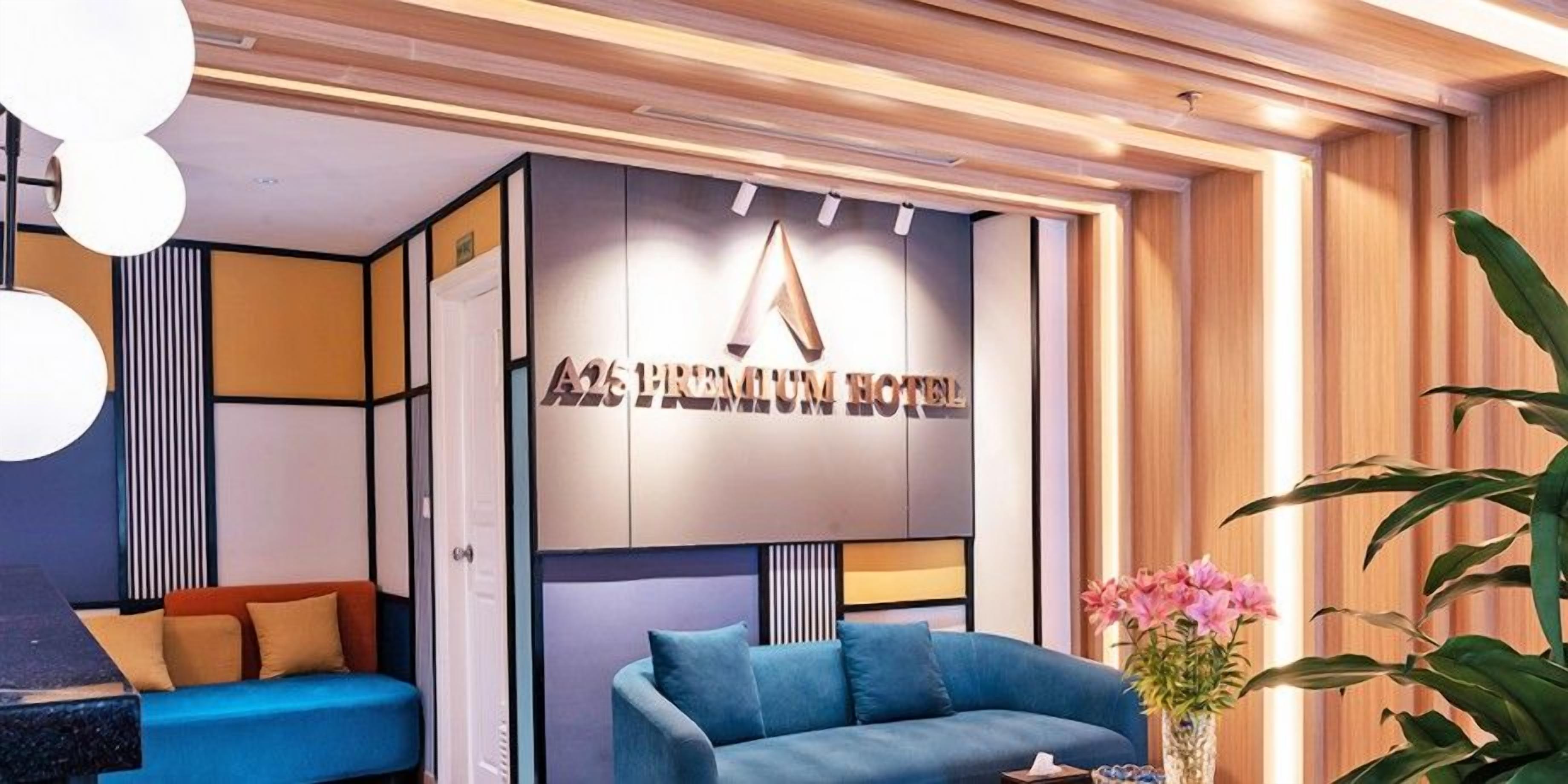 A modern hotel lobby with a blue sofa, a potted plant, and a wall-mounted sign reading 'A25 PREMIUM HOTEL'.