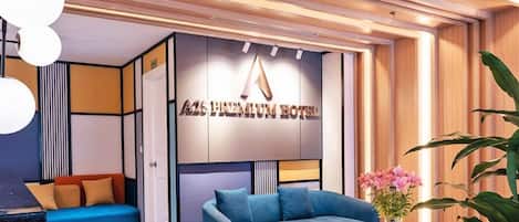 En modern hotellobby med en blå soffa, en krukväxt och en väggmonterad skylt med texten ”A25 PREMIUM HOTEL”.