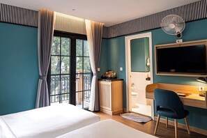 Een hotelkamer met een bed, een bureau, een stoel, een televisie, een ventilator en uitzicht op de omgeving.