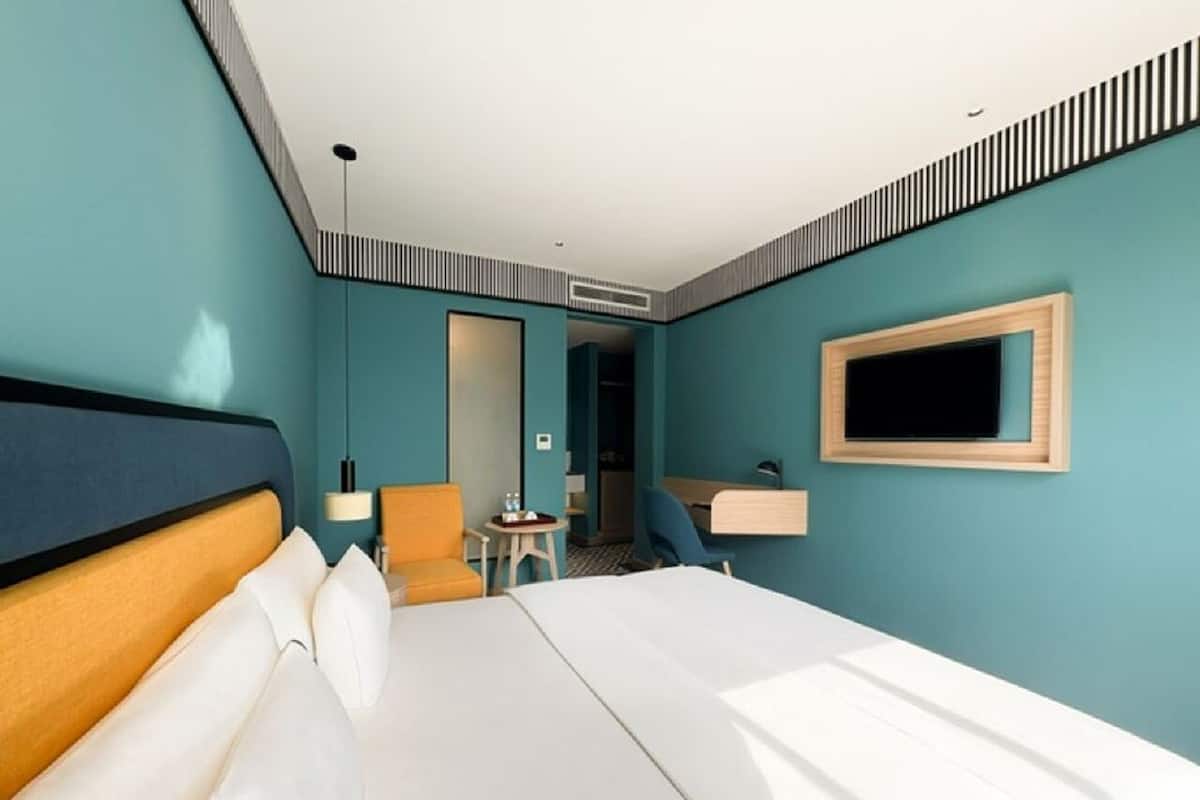 Ein Hotelzimmer mit einem großen Bett, einem Schreibtisch, einem Sessel, einem Fernseher und einer Tür zu einem weiteren Raum.