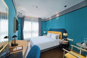 Une chambre d’hôtel comprenant un lit, des tables de chevet, un bureau avec un ordinateur, une chaise et une fenêtre avec des rideaux.