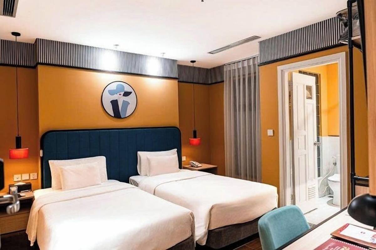 Ein Hotelzimmer mit zwei Betten, einem Schreibtisch, einem Stuhl, einem Nachttisch, einer Lampe, einem Spiegel und einer Tür zu einem Badezimmer.