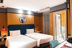 A hotel room with two beds, a desk, a chair, a nightstand, a lamp, a mirror, and a door leading to a bathroom. - A25 Premium Hotel - 130 Ba Trieu (Hanoi)