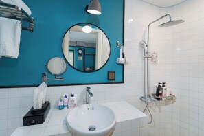 A bathroom with a white sink, a mirror, a towel rack, a shower, and toiletries.