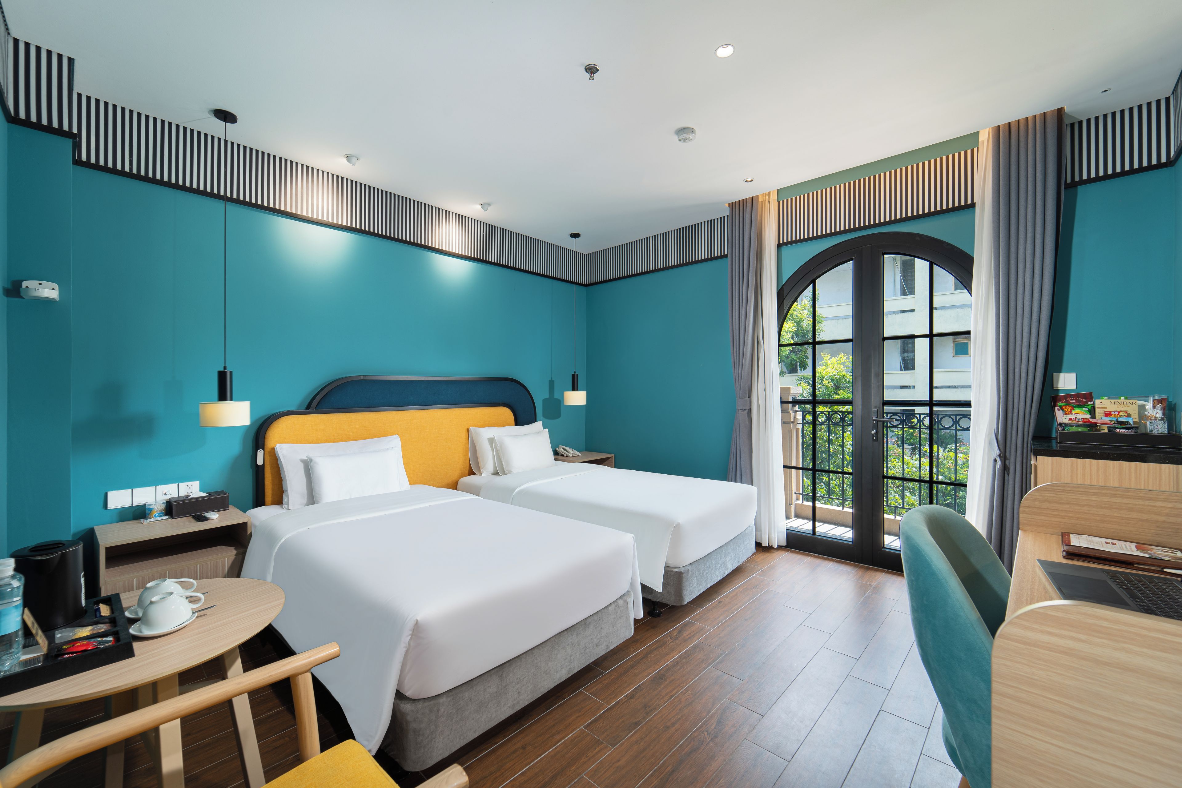 Une chambre d’hôtel avec deux lits, un bureau avec une chaise, une petite table et une vue sur la verdure.