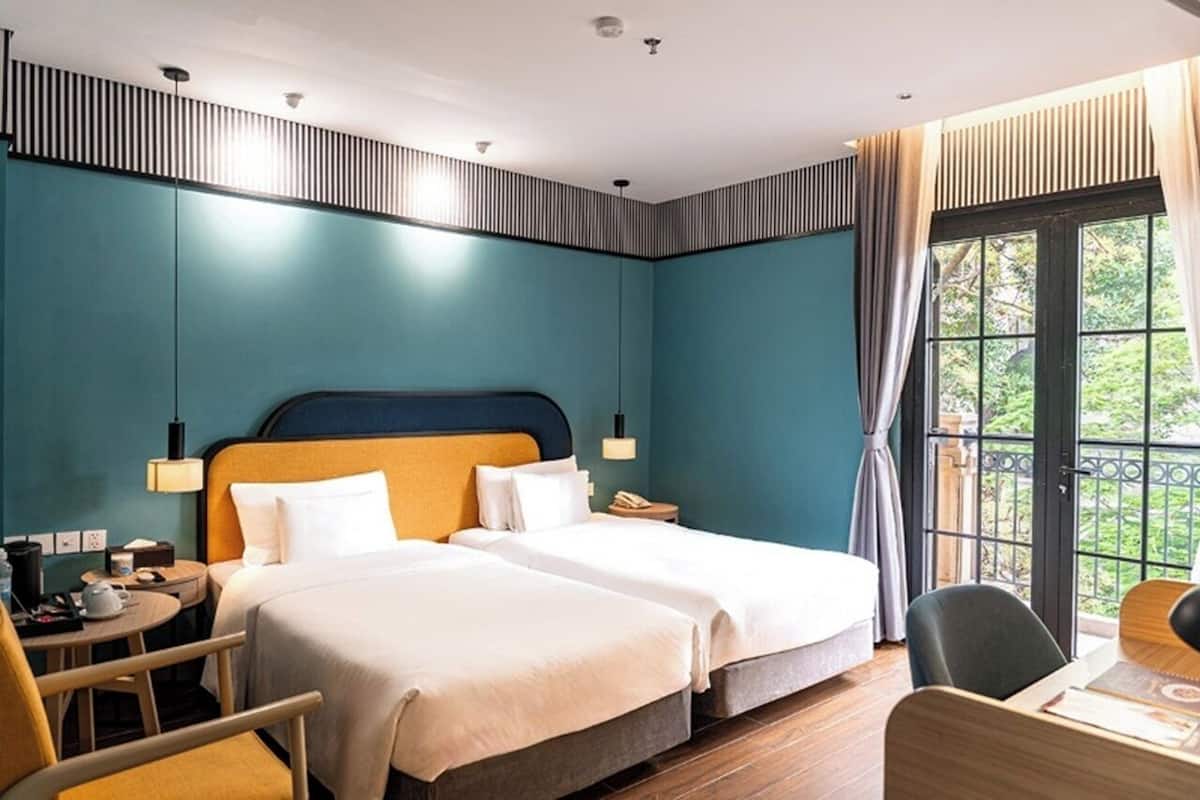 Ein Hotelzimmer mit zwei Betten, einem Schreibtisch, einem Sessel und einem Balkon mit Blick.
