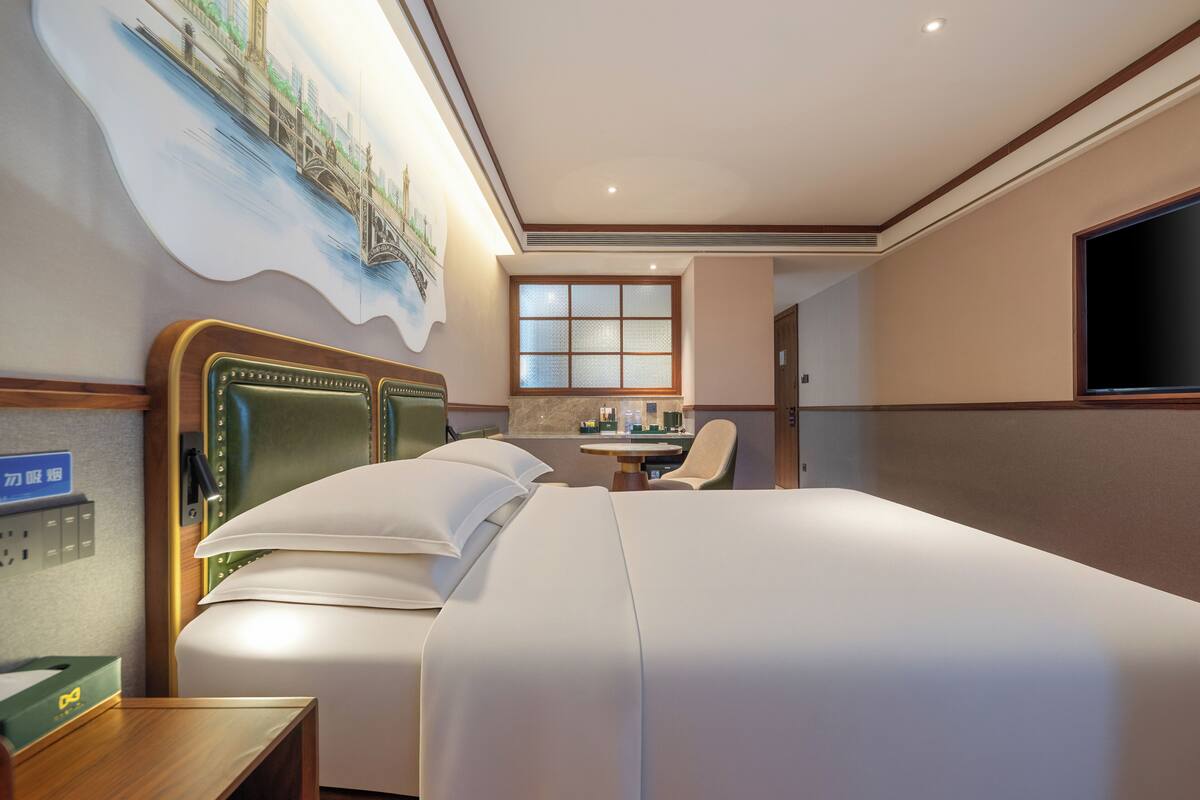 Habitación de hotel con una cama grande, un escritorio, una silla, un televisor y un cuadro en la pared.