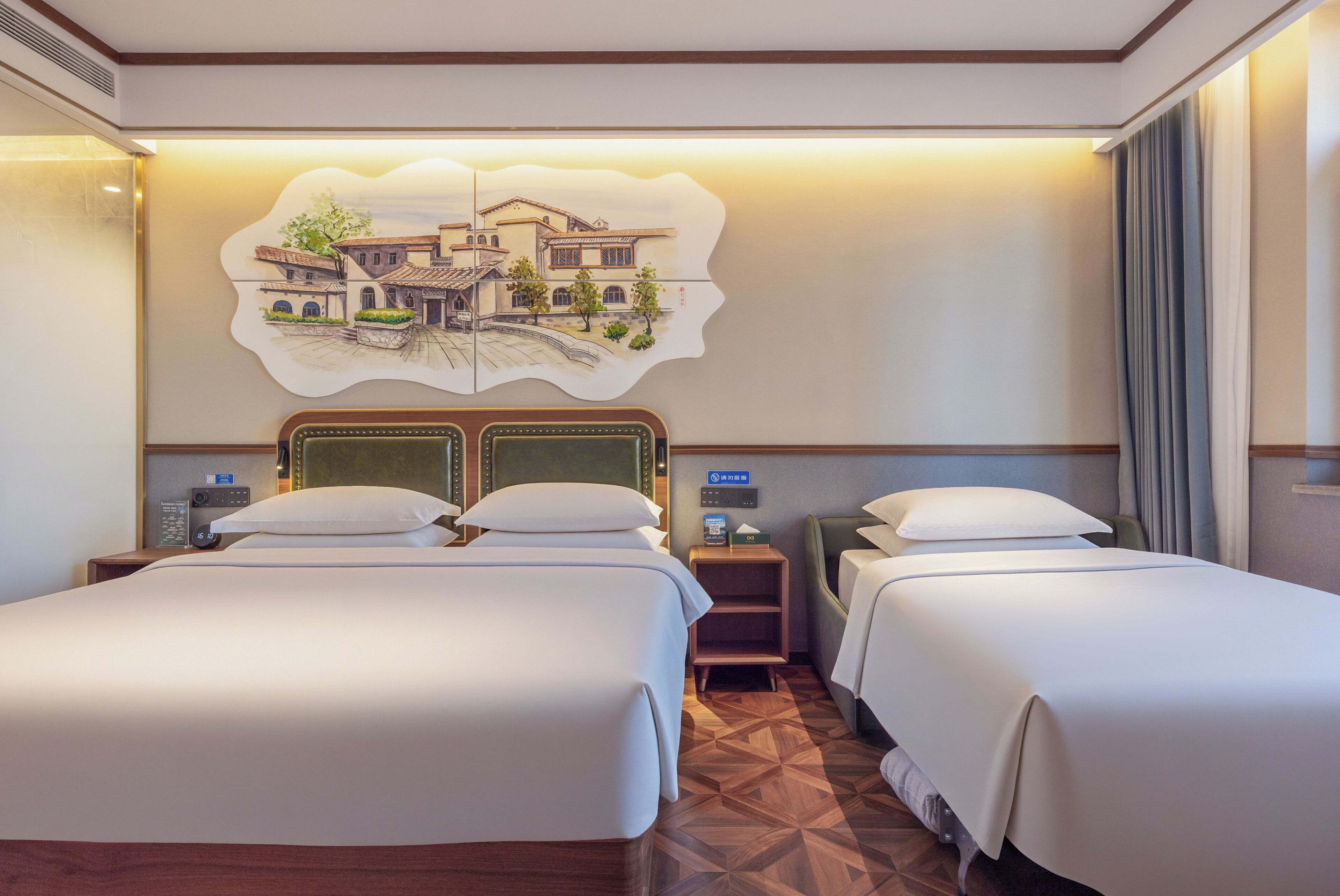 Quarto de hotel com duas camas, piso de madeira, obra de arte na parede, mesa de cabeceira com telefone e uma pequena mesa com abajur.