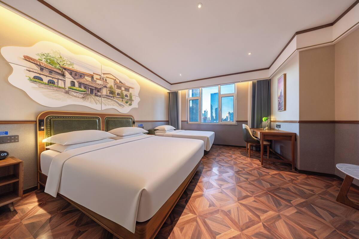 Habitación de hotel con dos camas, un escritorio, una silla y un ventanal con vistas a la ciudad.