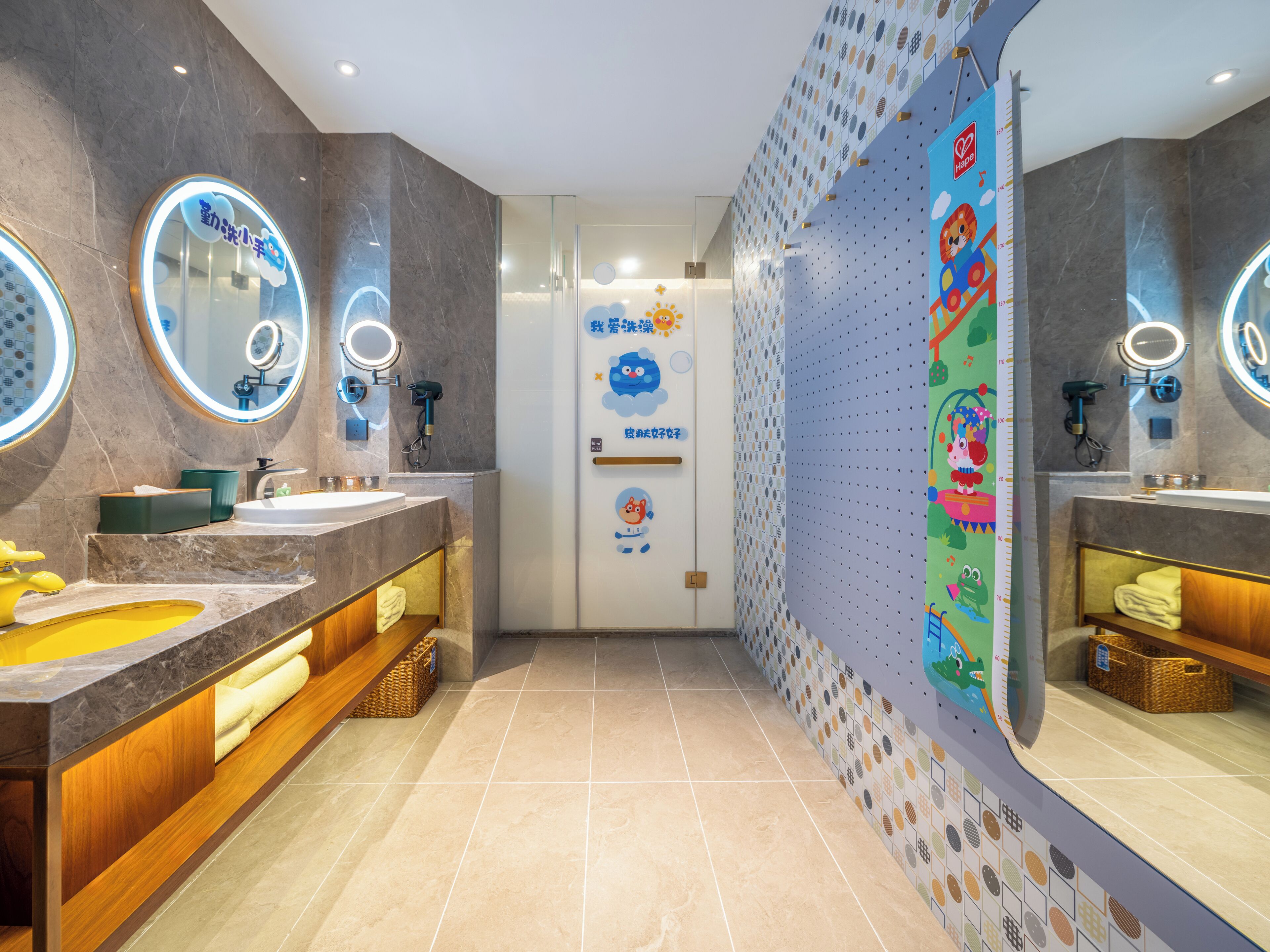 A modern bathroom with dual sinks, vanity mirrors, and a children's play area wall.