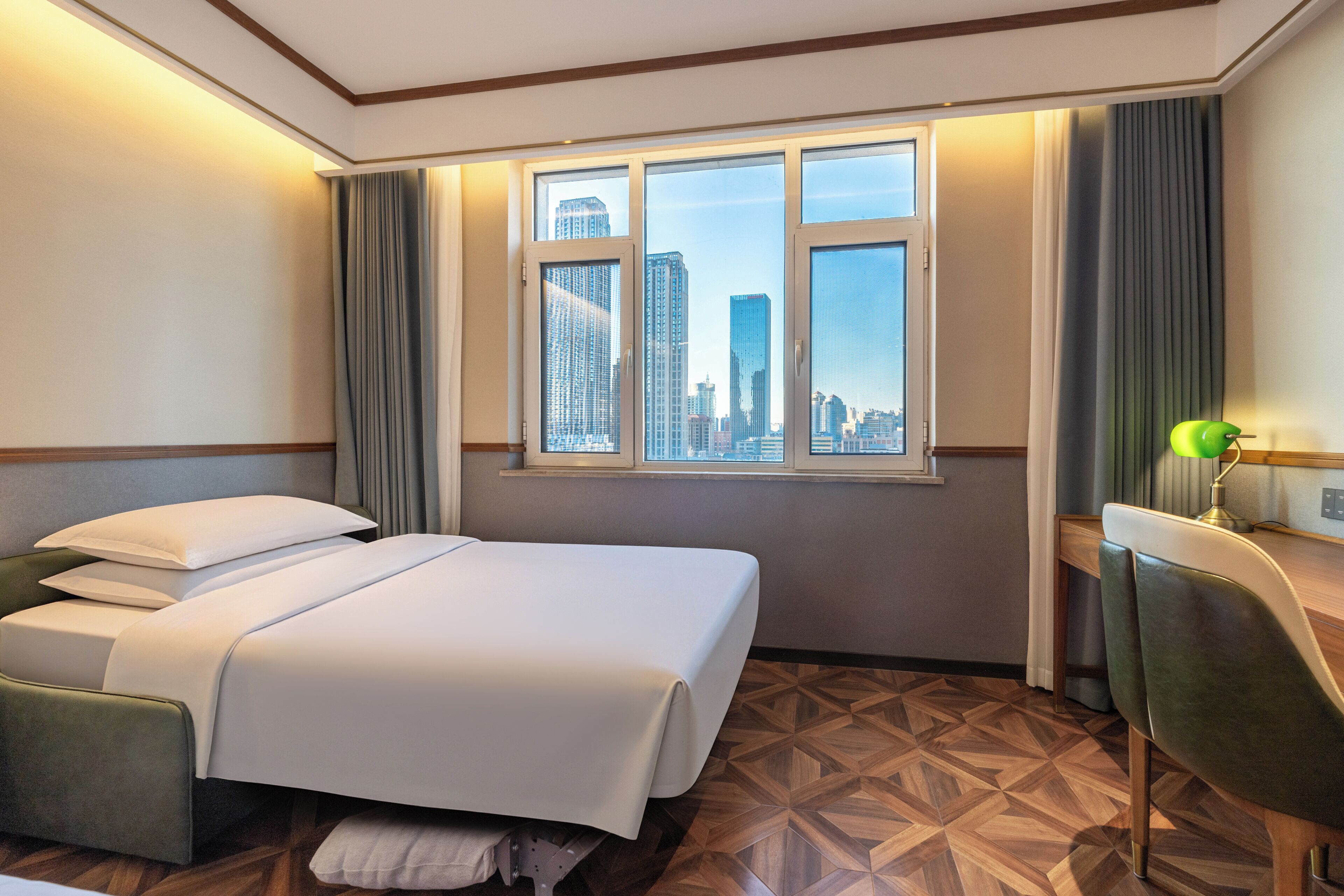 Habitación de hotel con cama, escritorio, silla y ventana con vista a la ciudad.