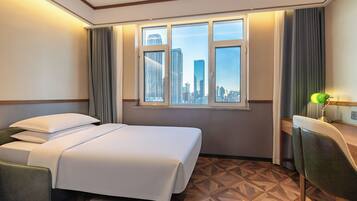Habitación de hotel con cama, escritorio, silla y ventana con vista a la ciudad.