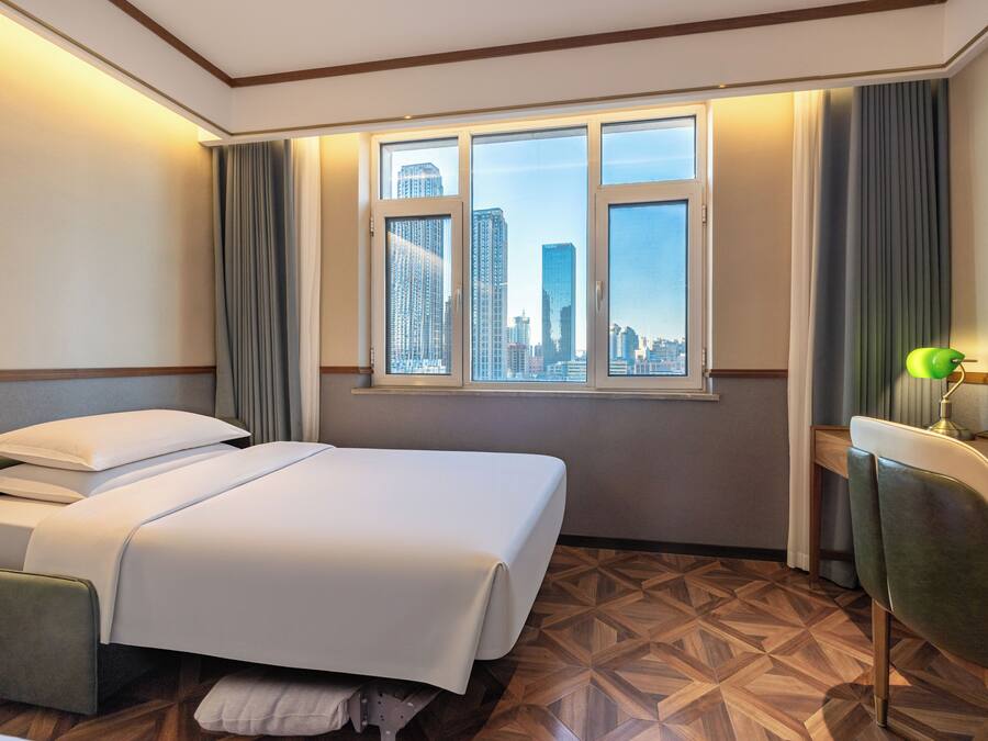 Habitación de hotel con cama, escritorio, silla y ventana con vista a la ciudad.