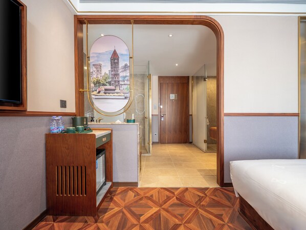 Habitación de hotel con un escritorio de madera, un espejo, una cama y vistas de un paisaje urbano a través de un espejo circular.