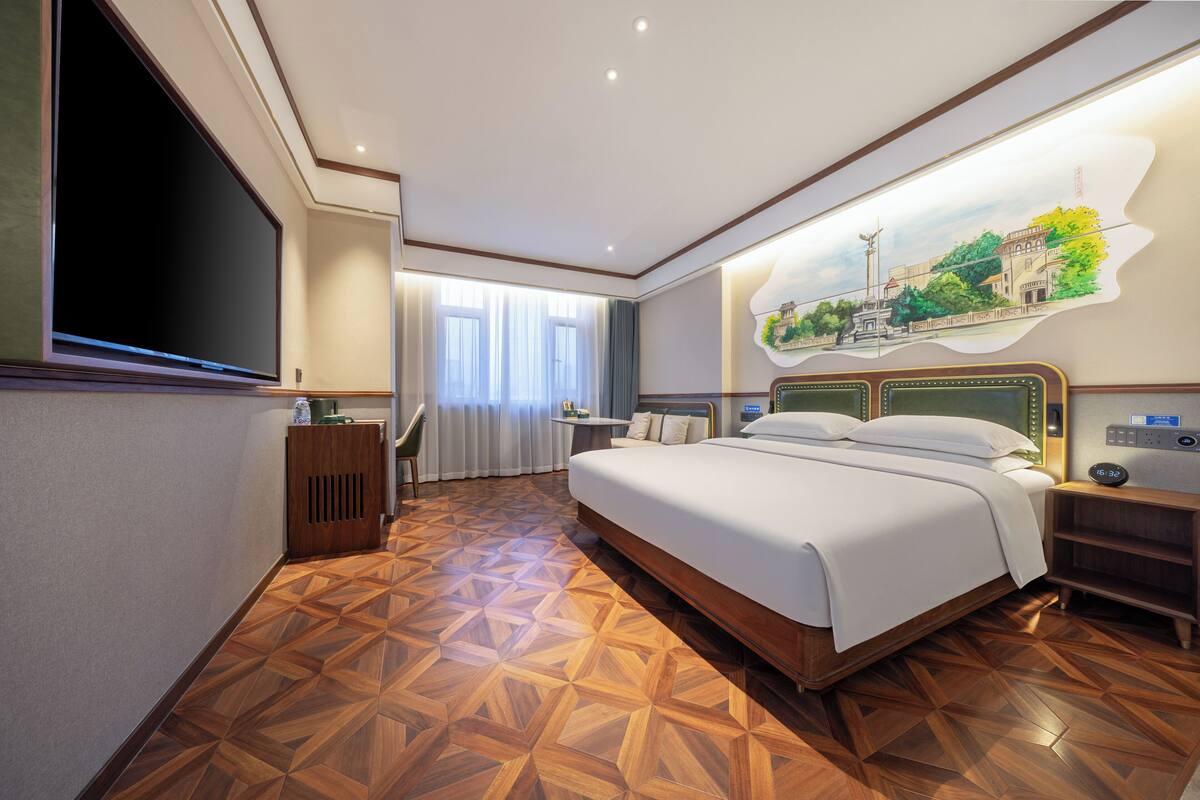 Habitación de hotel con una cama grande, un televisor de pantalla plana, piso de parqué de madera y un mural en la pared.