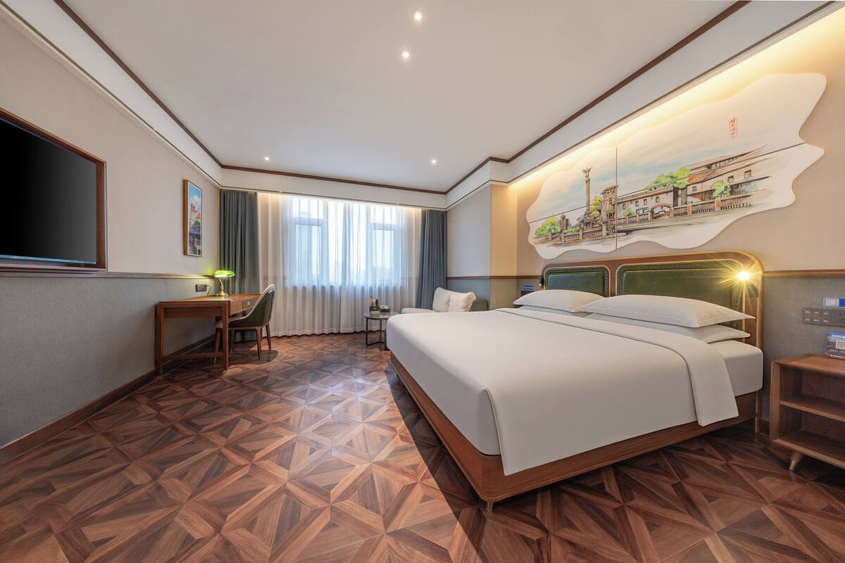 Habitación de hotel con una cama grande, un escritorio, una silla, un televisor y un mural en la pared.