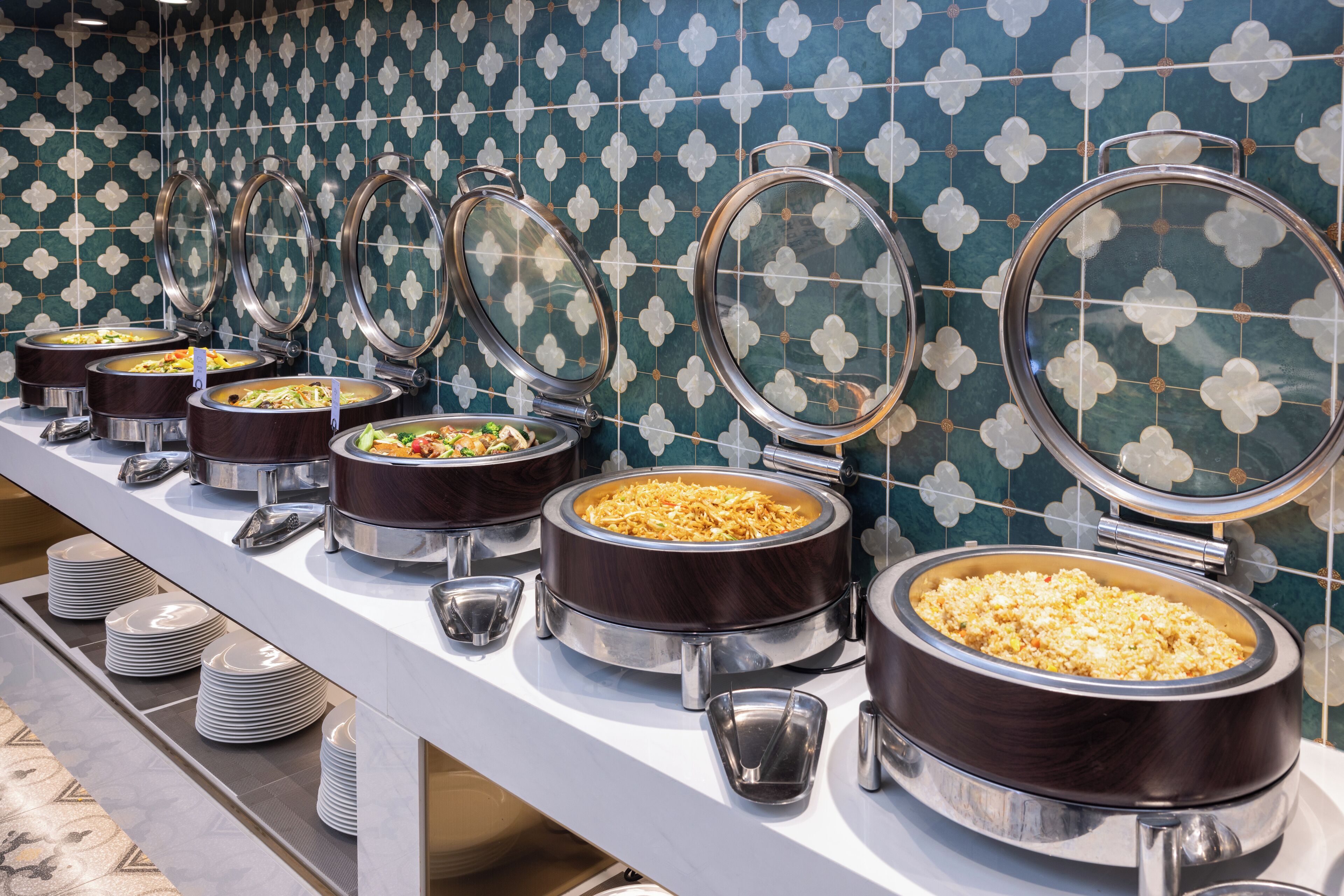 Una mesa de buffet con varias estaciones de comida, cada una con tapa y bandeja de servicio.