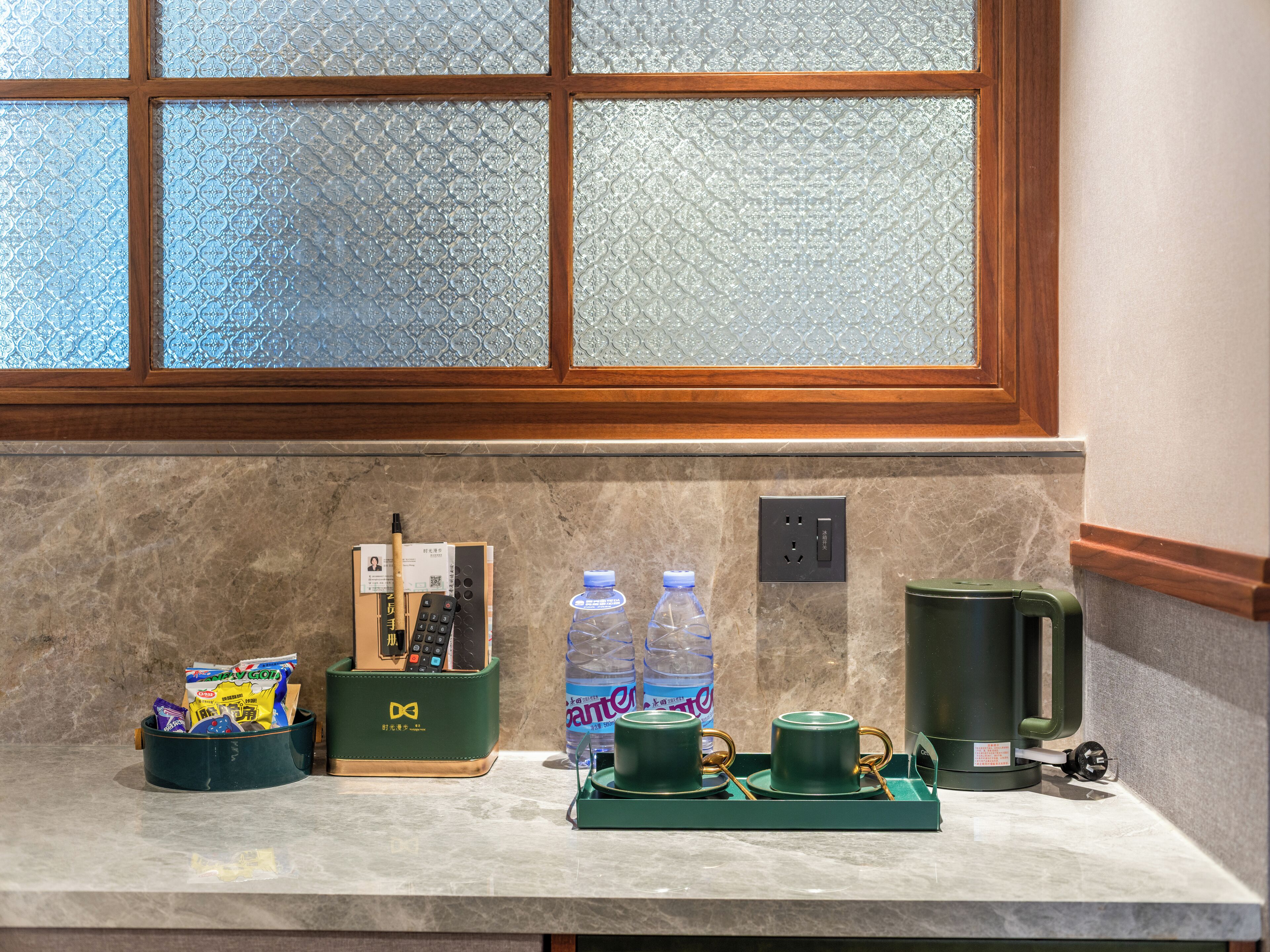 A kitchen counter with a coffee maker, a water bottle, and a green tray with cups.