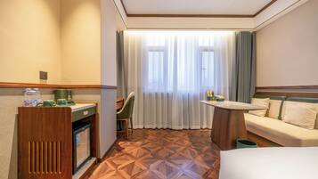 A hotel room with a wooden floor, a desk with a chair, a sofa, and a bed.