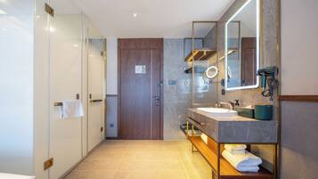 A modern bathroom with a glass shower enclosure, a wooden door, a vanity with a mirror, and a towel rack.