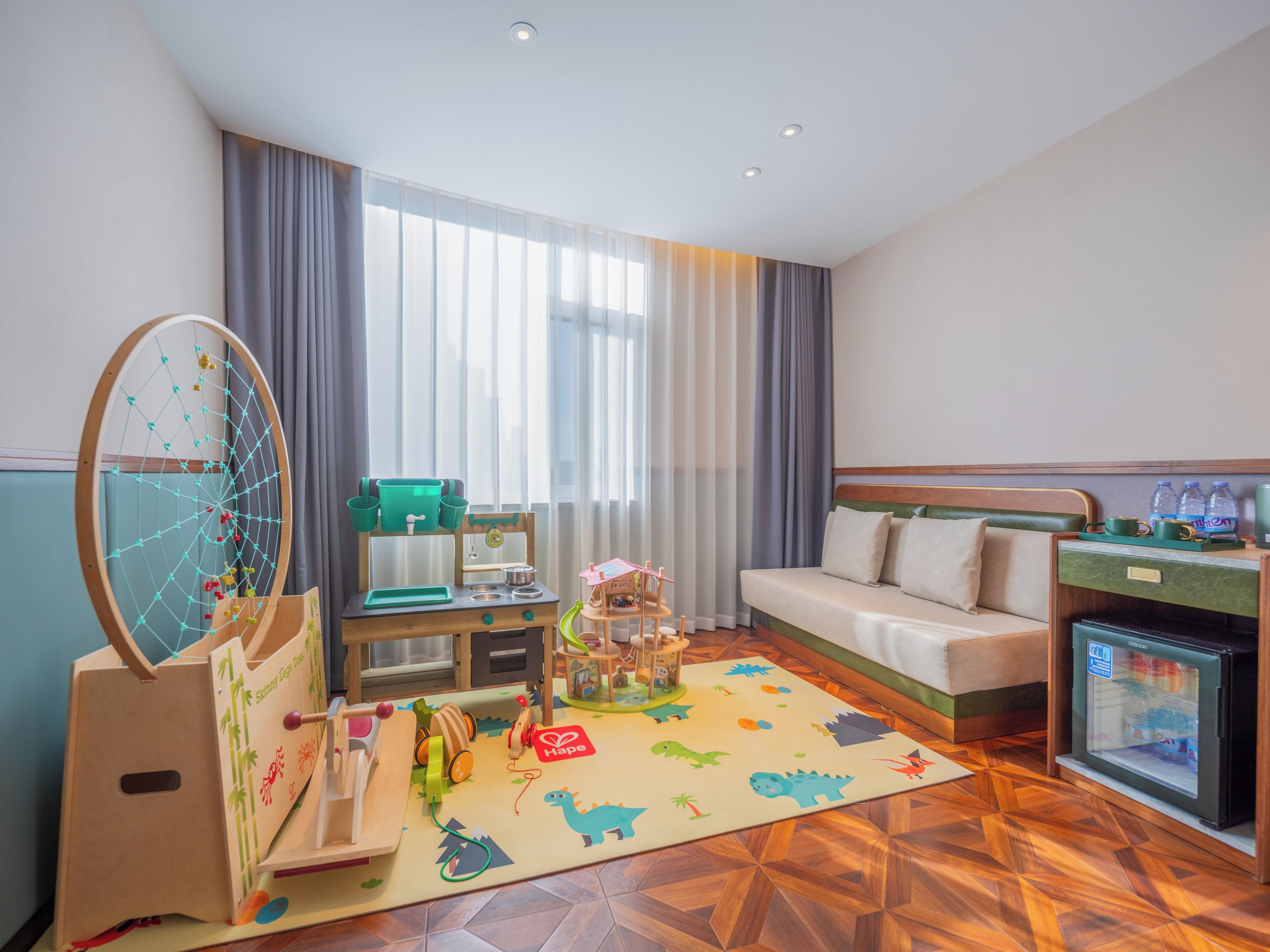 Une chambre d’hôtel équipée d’un espace de jeux en bois, d’un canapé, d’un lit et d’un mini-bar.