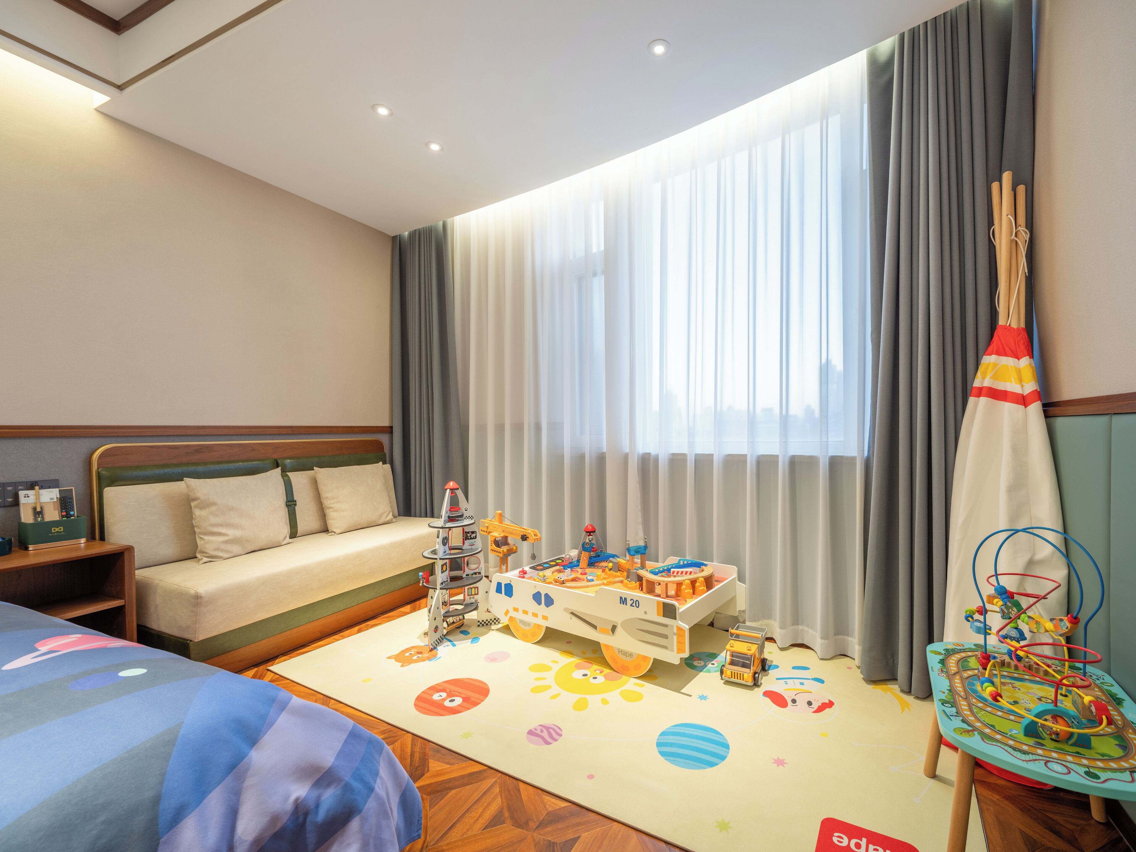 Une chambre d’hôtel comprenant un lit, un canapé, un espace de jeux avec des jouets et une fenêtre avec des rideaux.