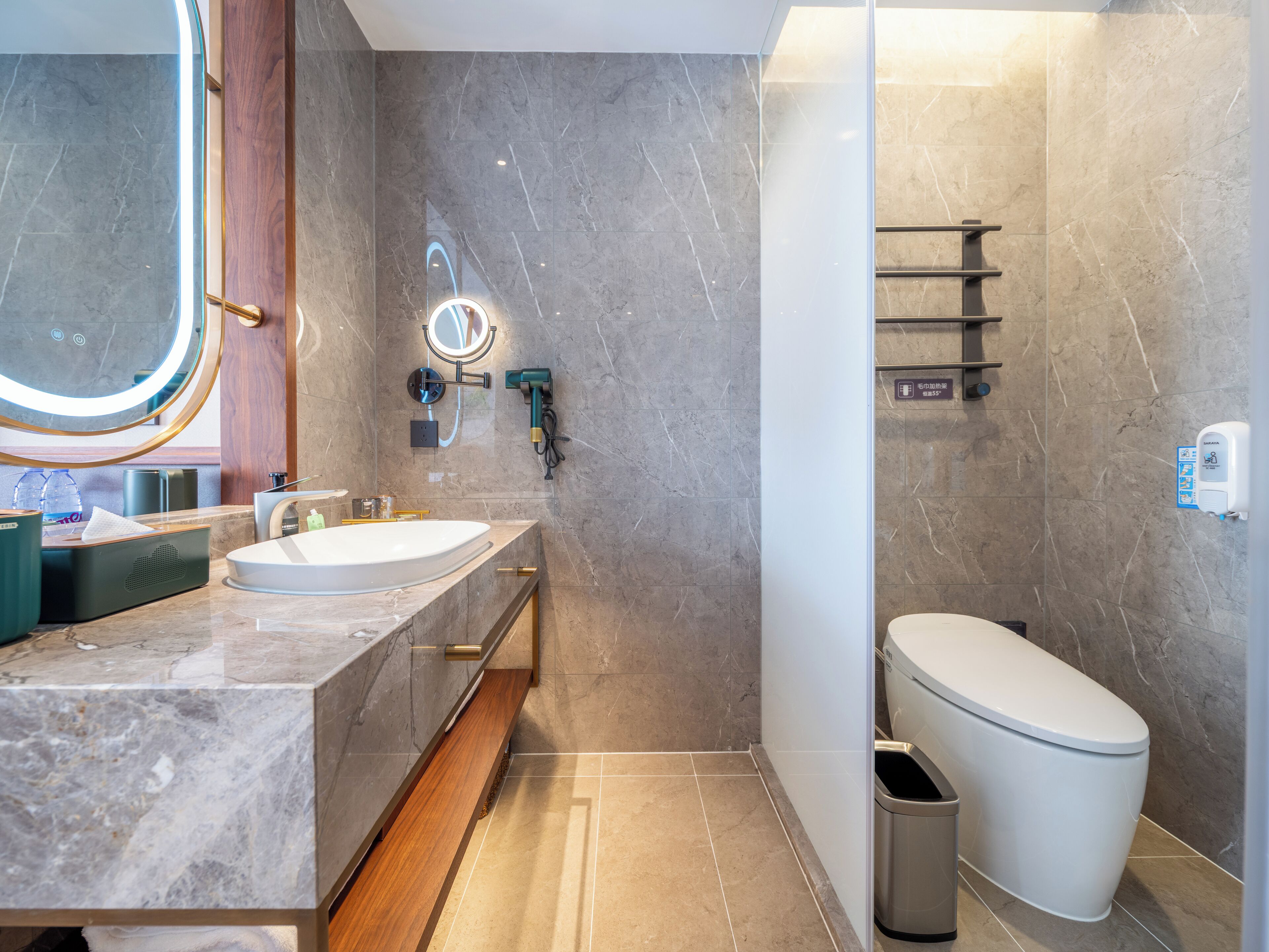 A modern bathroom with a marble vanity, a round mirror, a handheld showerhead, and a toilet.