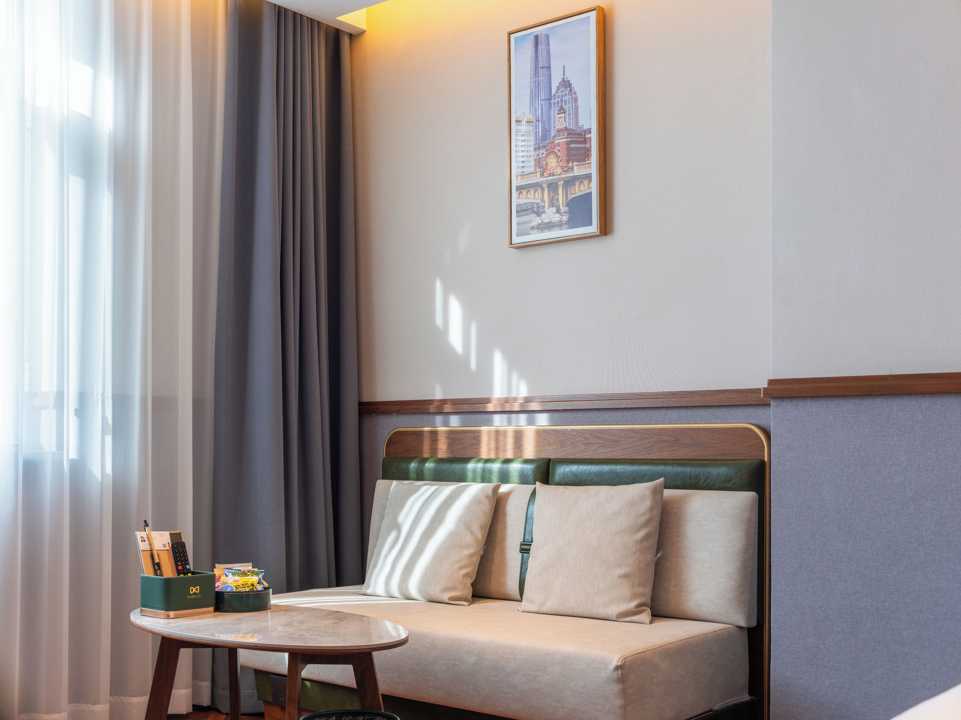 A hotel room with a sofa, a small table, a framed picture on the wall, and a window with curtains.