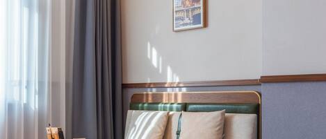 A hotel room with a sofa, a small table, a framed picture on the wall, and a window with curtains.