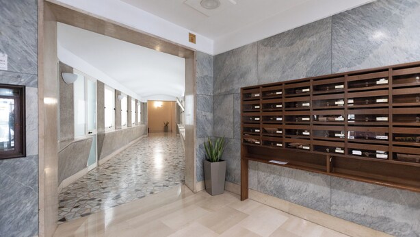 A hallway with a marble floor, a plant in a grey planter, and a wooden display rack with items. - Macedonia 30 Bright Flat (Rome)