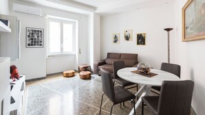 A modern dining area with a round table, brown chairs, and a white ceiling. - Macedonia 30 Bright Flat (Rome)