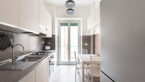 A modern kitchen with white cabinets, a stainless steel sink, and a dining area with a white table and chairs. - Macedonia 30 Bright Flat (Rome)