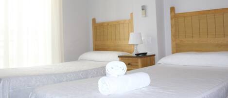 Habitación de hotel con dos camas, cabecero de madera, mesita de noche con lámpara y una toalla enrollada sobre la cama.