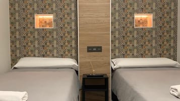 Habitación de hotel con dos camas, papel tapiz estampado e iluminación adosada a la pared.