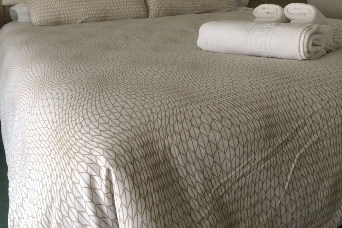 Un lit bien fait, avec une couvre-lit à motifs, deux oreillers et une serviette pliée posée sur le côté.