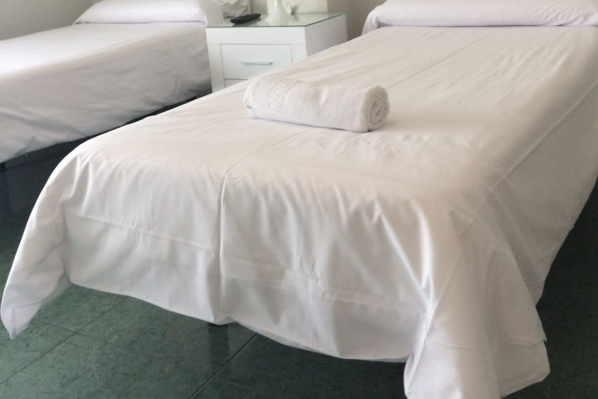 Une chambre d’hôtel avec deux lits simples, une table de chevet avec une lampe et un tableau représentant une voiture, accroché au mur.