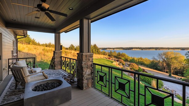 Una terraza cubierta con chimenea de piedra, mobiliario exterior y vistas a un lago y el paisaje circundante.