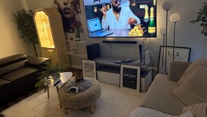 Een moderne woonkamer met een grote flatscreen-televisie, een comfortabele bank, een klein rond poefje en een decoratieve plant.