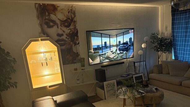 Een moderne woonkamer met een flatscreen televisie, een glazen kast met flessen, een bank en een salontafel.