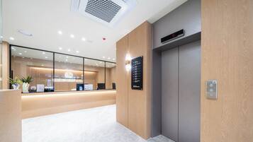 A hotel reception area with a modern design, a reception desk, a digital clock, and an elevator.