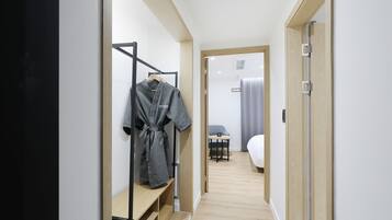 A hallway with a wooden bench, a clothing rack with a robe, and a glimpse of a bed and a table in the distance.