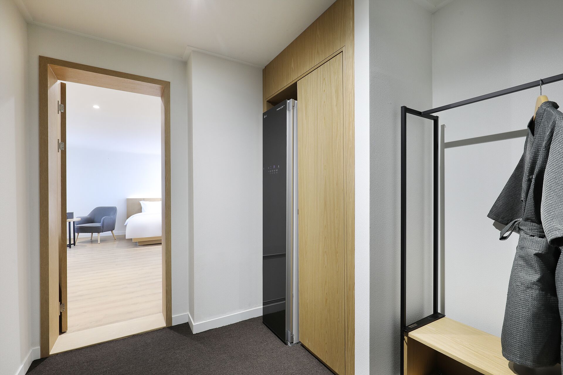 A modern hotel room with a wooden wardrobe, a black-framed mirror, and a grey carpet.