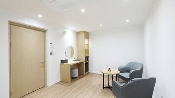 Une chambre moderne avec une porte en bois, un bureau doté d’un miroir, une petite table ronde et deux chaises grises.