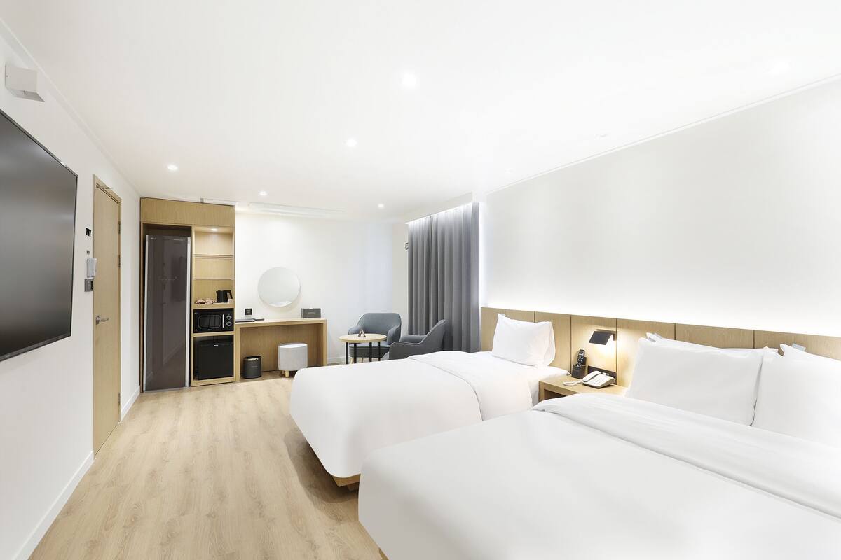 A modern hotel room with two beds, a desk, a chair, a microwave, a coffee maker, and a TV.