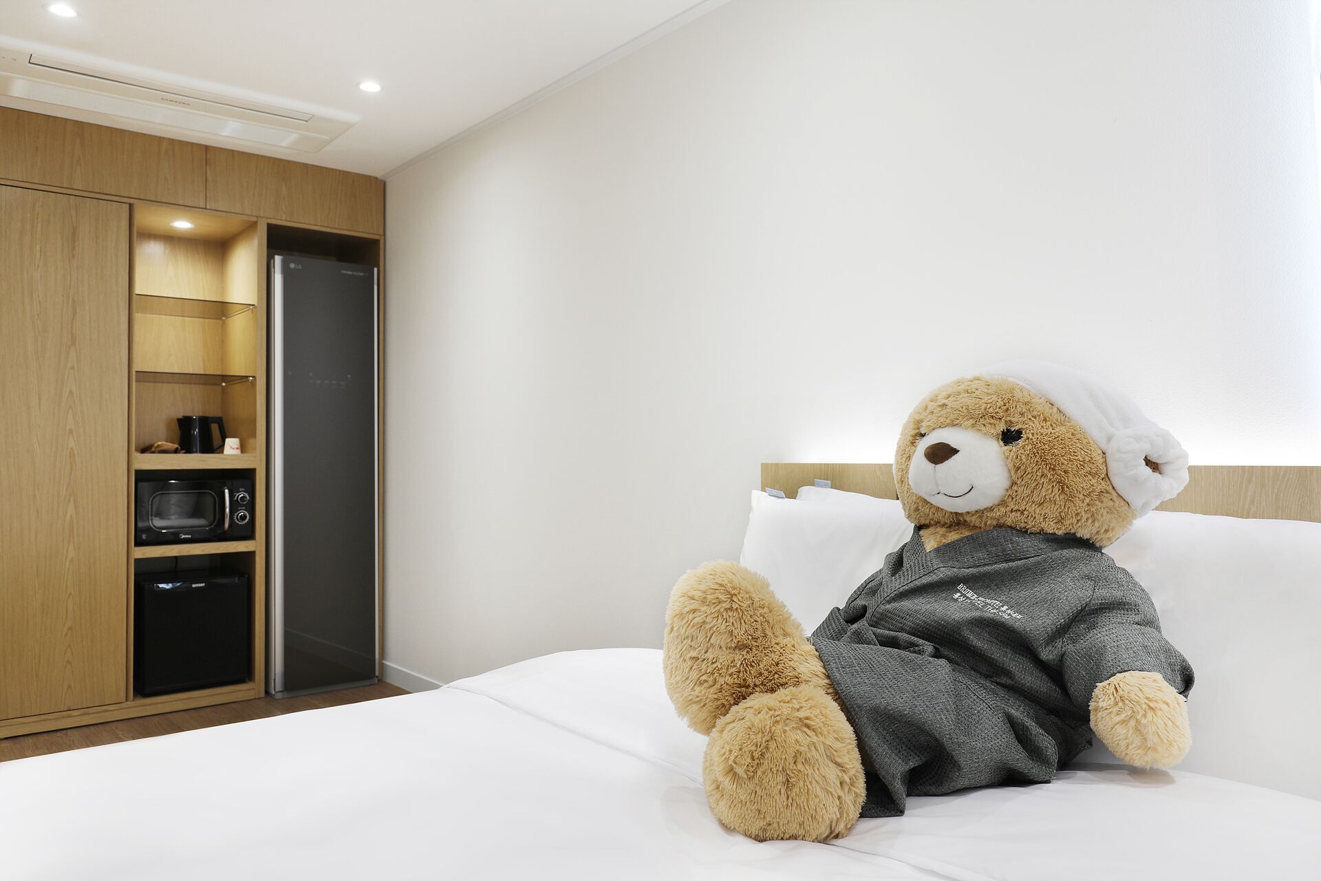 A hotel room with a bed, a teddy bear, a wardrobe, and a microwave.
