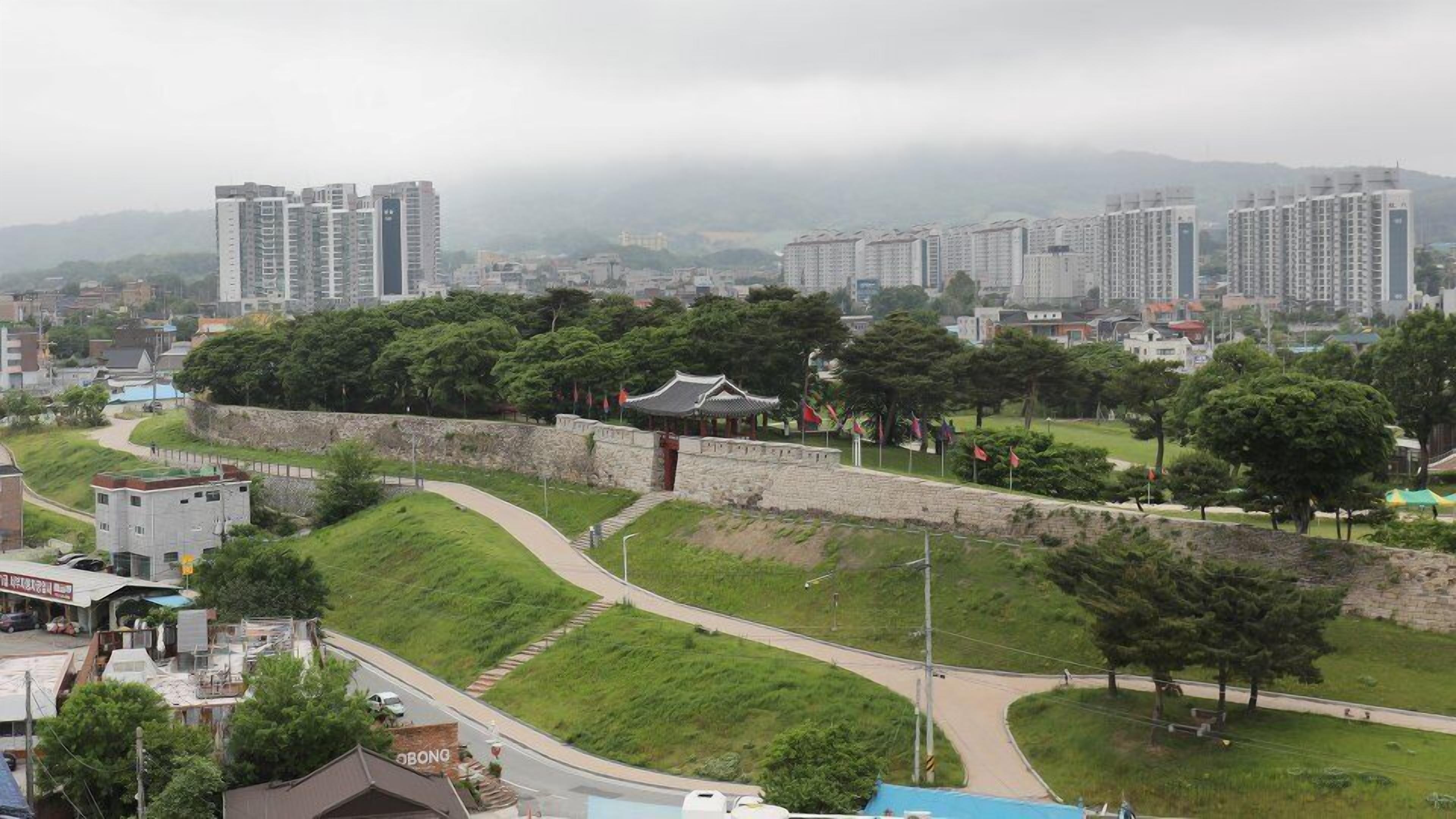 A traditional Korean-style pavilion surrounded by a stone wall, with modern high-rise buildings in the background.
