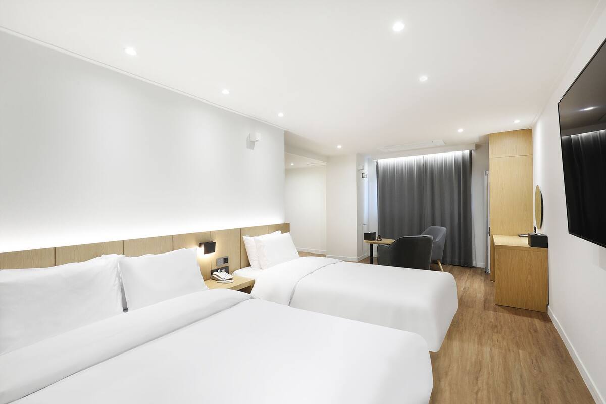 A hotel room with two beds, a desk, a chair, a TV, and a bathroom with a shower and toilet.