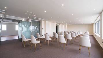 A conference room with rows of white chairs, a glass partition, and a large window.