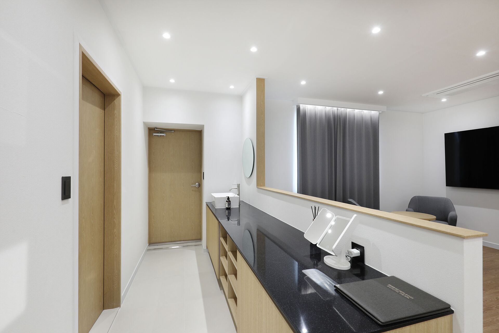 A modern bathroom with a wooden door, a mirror, a sink, and a toilet.