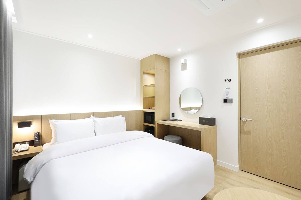 A hotel room with a bed, bedside table, lamp, and a wooden wardrobe.